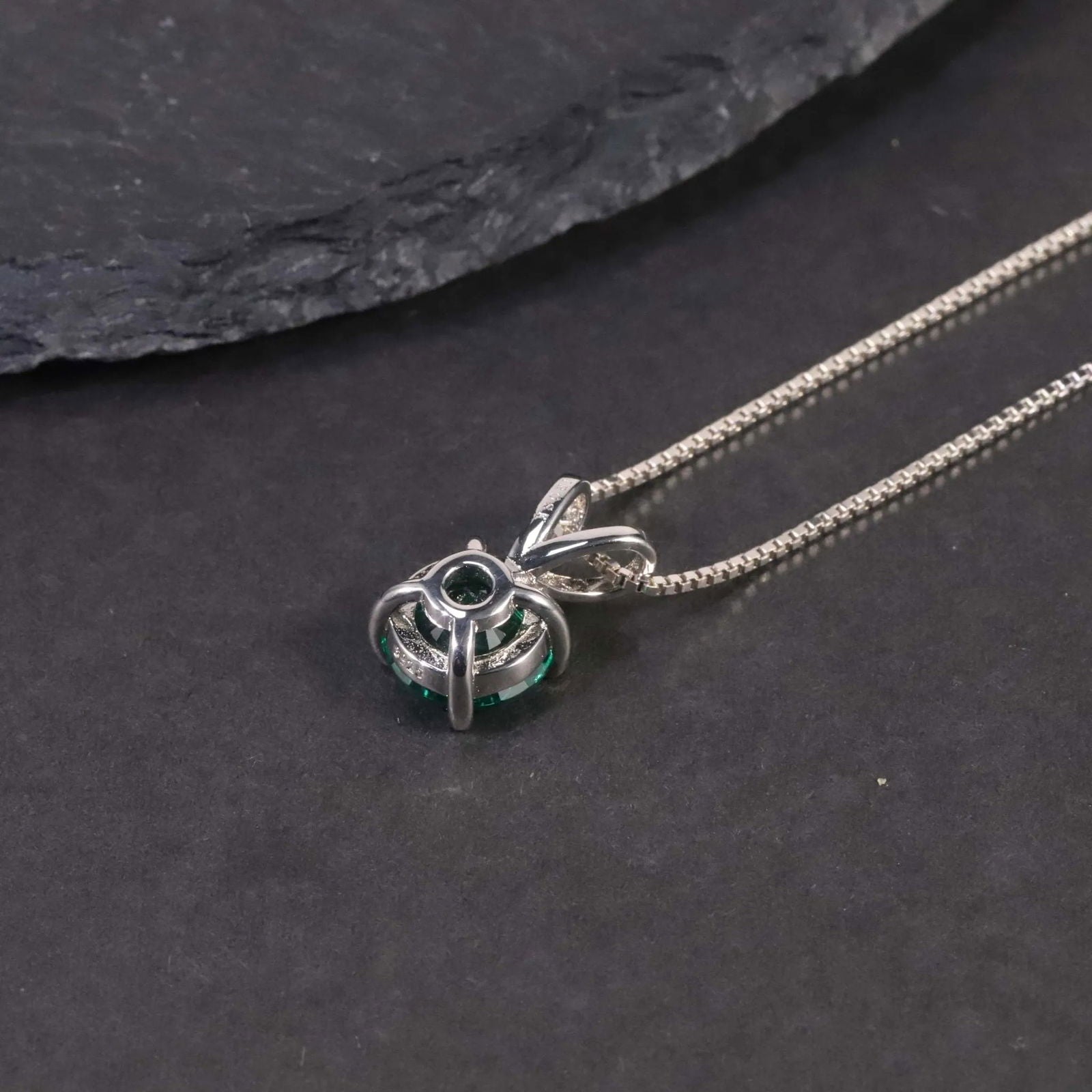 Alternate angle showing the round emerald pendant necklace against a dark surface.