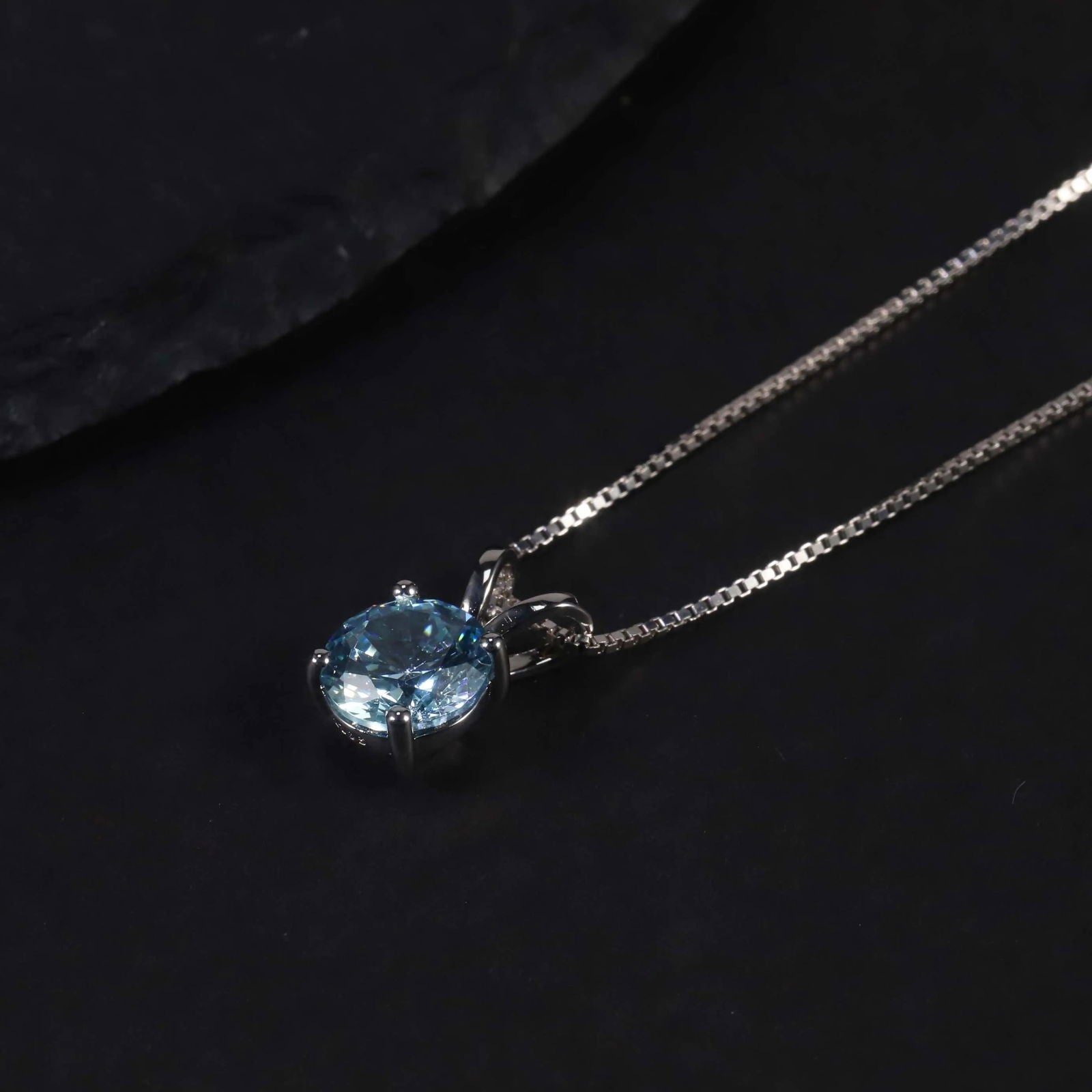 Silver aquamarine pendant displayed against a black backdrop, highlighting its round-cut stone and shine.