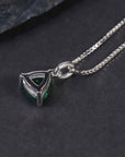Alternate angle showing the trillion-cut emerald pendant necklace against a dark surface.