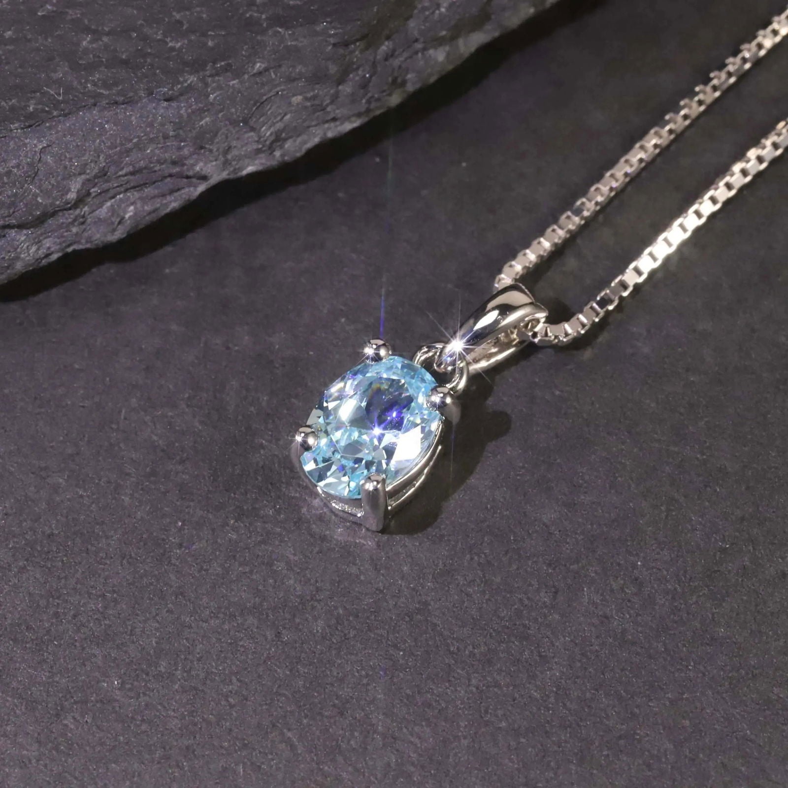 Close-up of the aquamarine pendant against a black backdrop, highlighting its oval cut and polished silver setting.