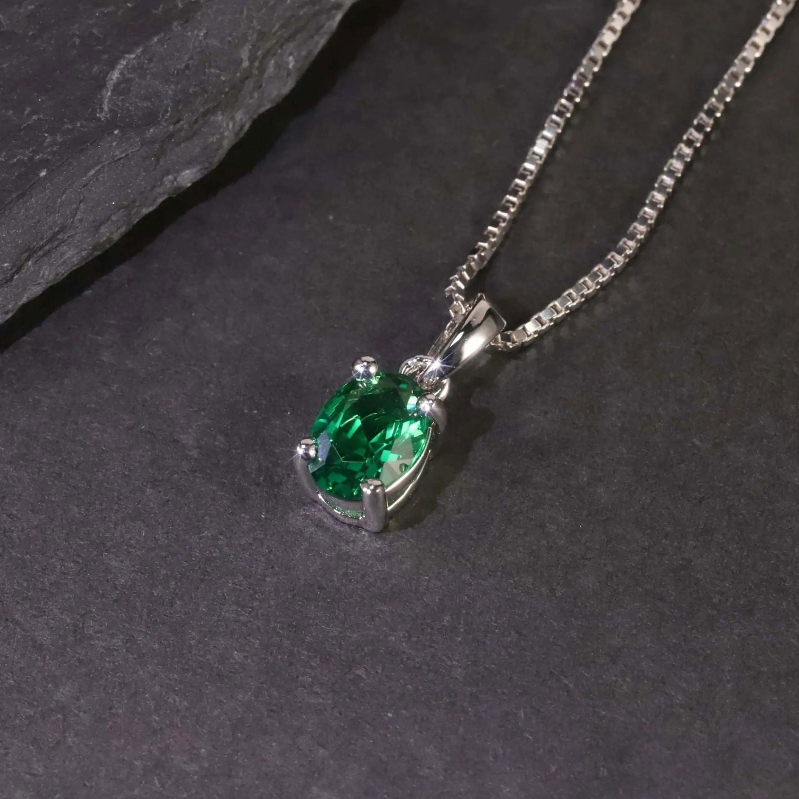 Close-up of the oval emerald pendant necklace displayed on a dark surface.”