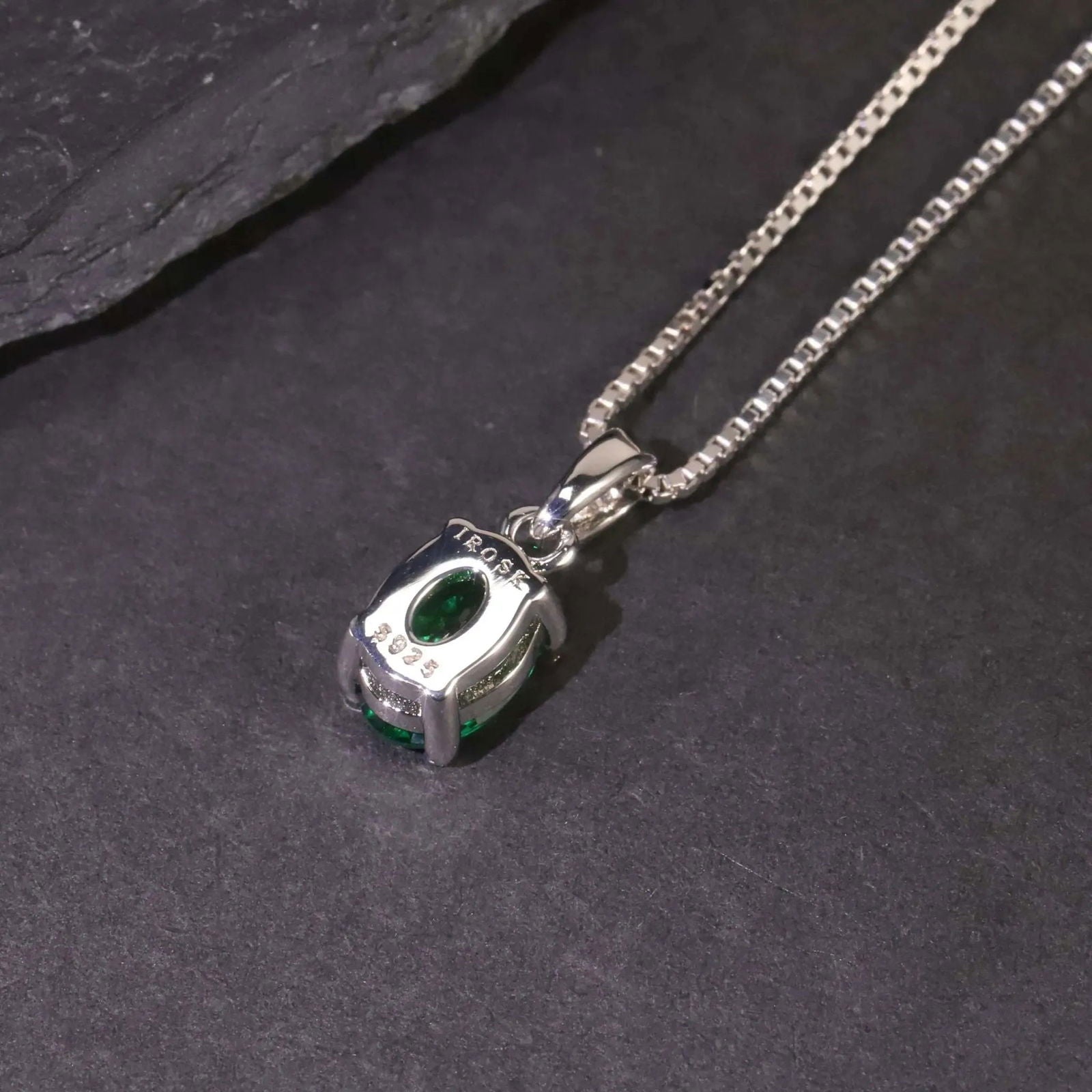 Alternate angle of the oval emerald pendant necklace against a dark surface.