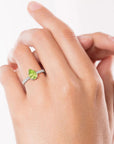Hand wearing a sparkling Pear Cut Peridot Ring, highlighting the gemstone's brilliance and elegant band adorned with side stones.