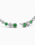 Angled view of the emerald climber earrings laid out, showing their prong settings and floral pattern.