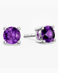 Pair of sterling-silver amethyst stud earrings with round, faceted purple gemstones—one shown from the front and the other at an angle to reveal the four-prong setting—displayed on a white background