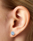 A close-up of a woman’s ear wearing a single aquamarine halo stud earring.