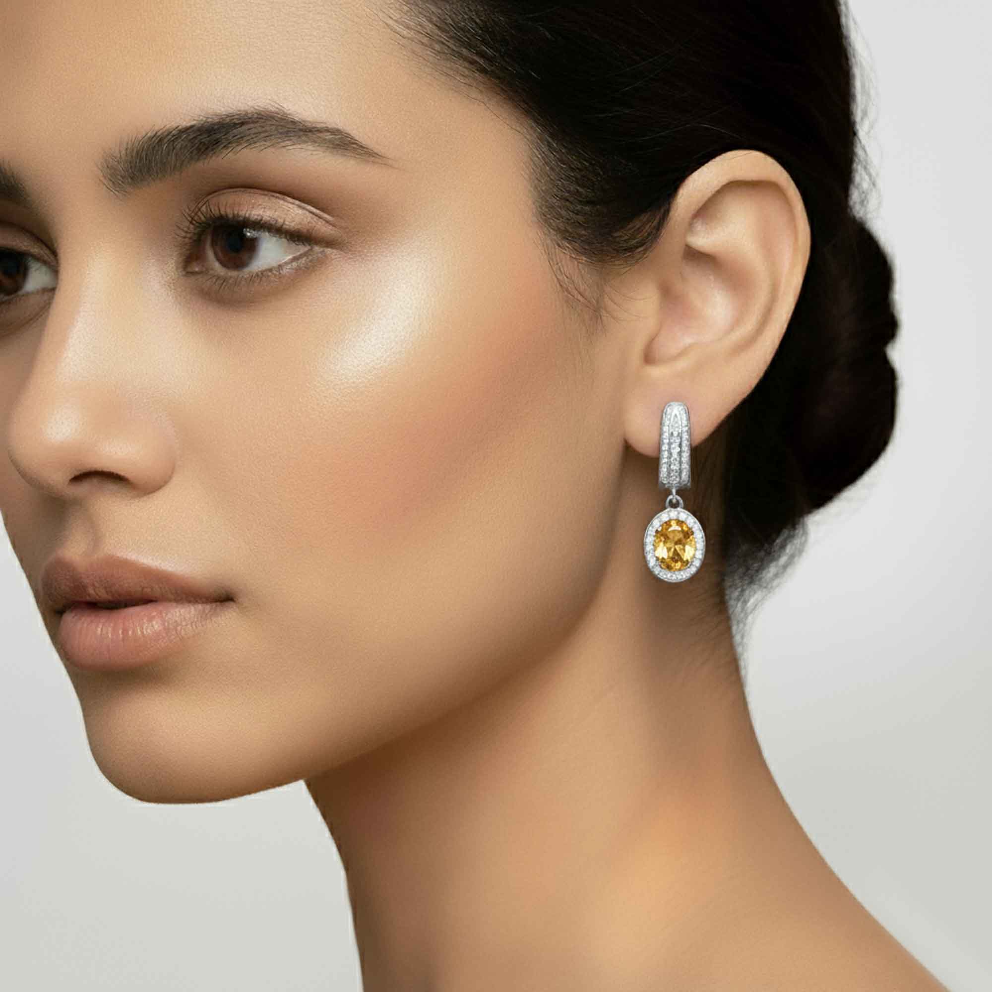 Close-up of a woman wearing a diamond earring with a yellow citrine gemstone on a neutral background