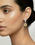 Close-up of a woman wearing a diamond earring with a yellow citrine gemstone on a neutral background