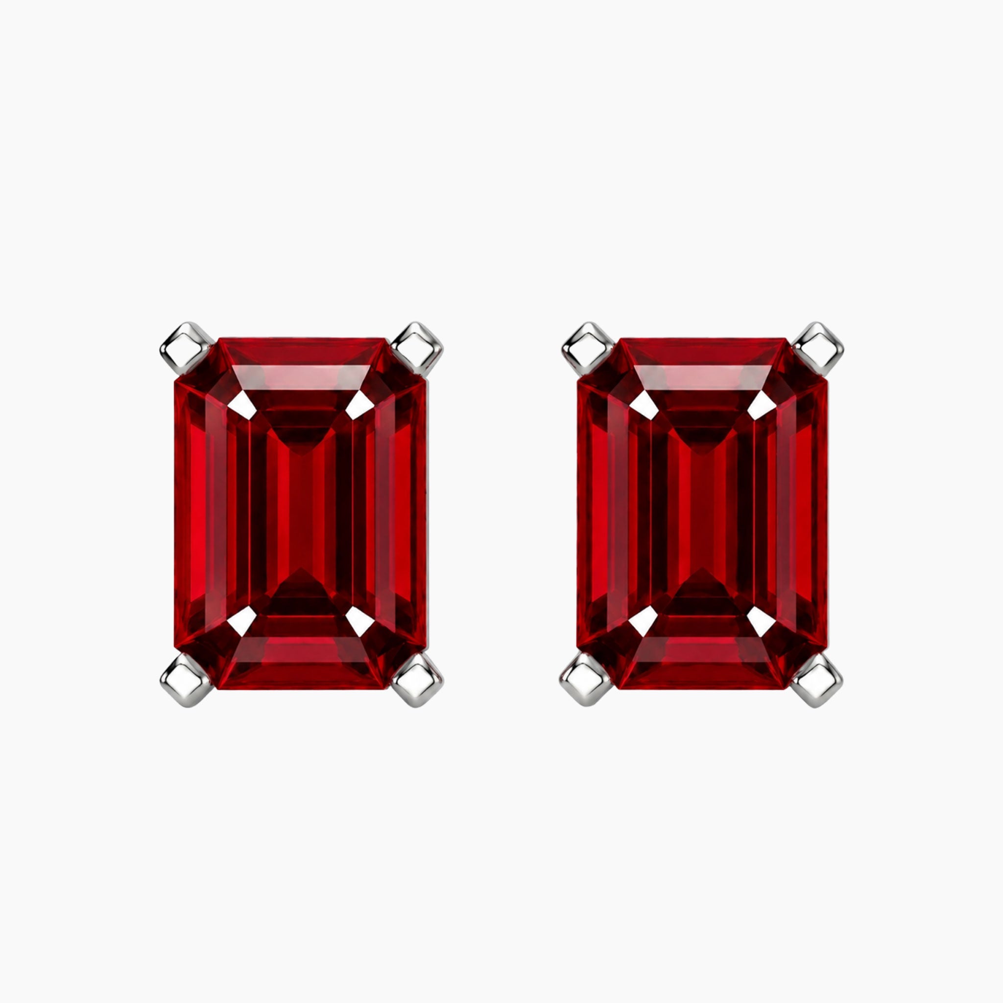 A pair of emerald-cut red ruby gemstone stud earrings in silver-toned prong settings, shown on a plain light gray background.