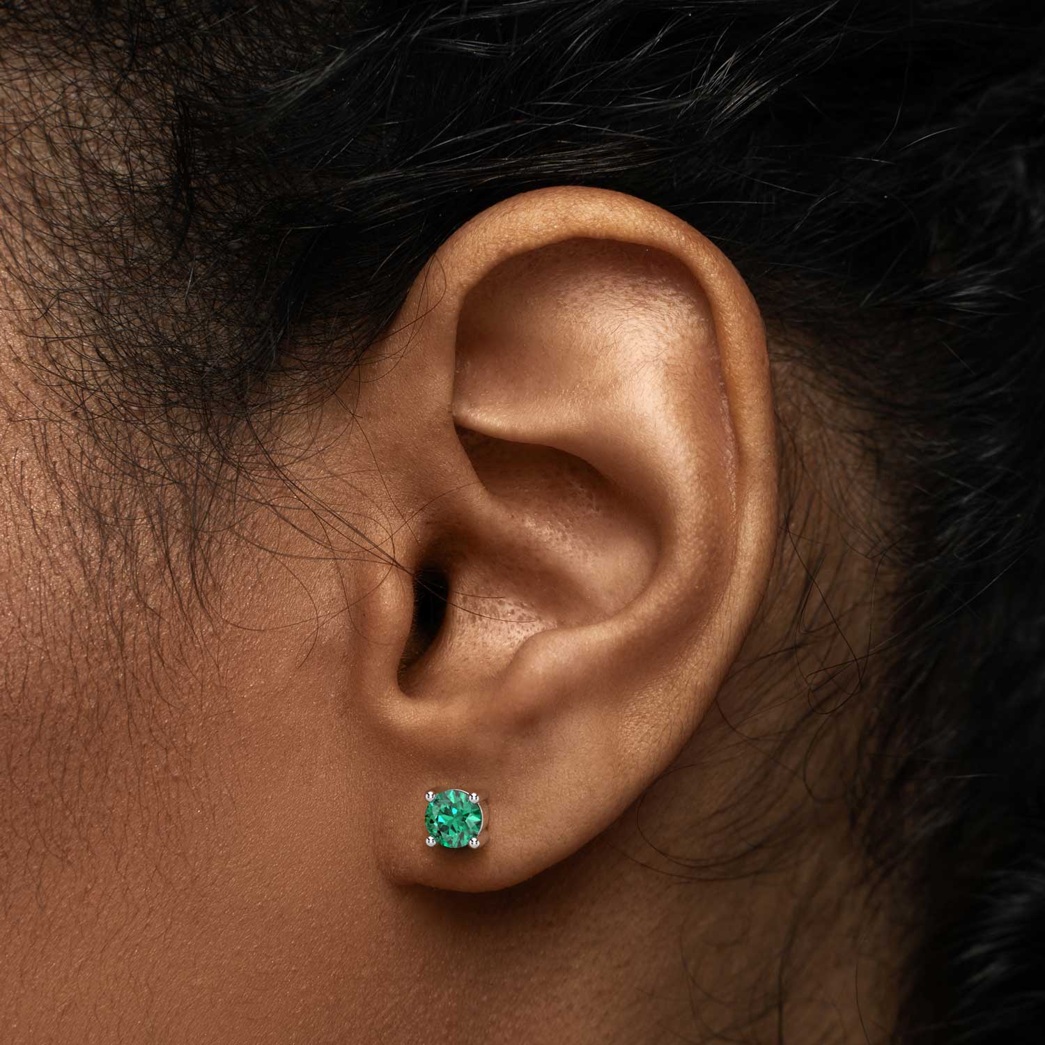 Close-up of a model’s ear wearing a round-cut emerald stud earring.