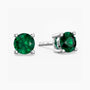 Sterling-silver stud earrings featuring round, faceted green emerald gemstones—one shown from the front and the other angled to reveal the four-prong setting and ‘S925’ hallmark on the post—against a white background.