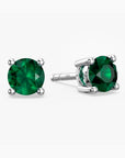 Sterling-silver stud earrings featuring round, faceted green emerald gemstones—one shown from the front and the other angled to reveal the four-prong setting and ‘S925’ hallmark on the post—against a white background.