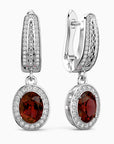 Pair of earrings with red garnet gemstones and diamond accents on a white background