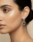 Close-up of a woman wearing a silver earring with a red garnet gemstone on a beige background