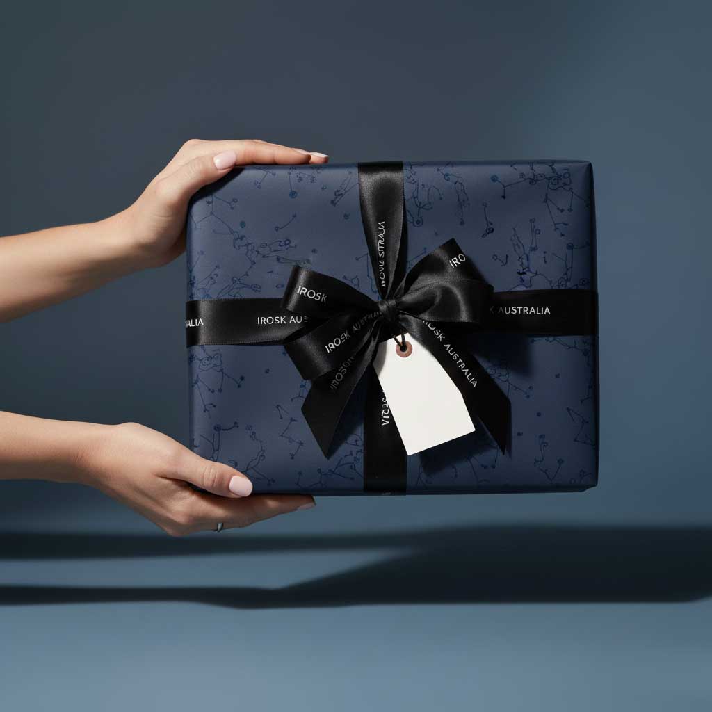 Navy gift box with black ribbon held by a hand against a dark background