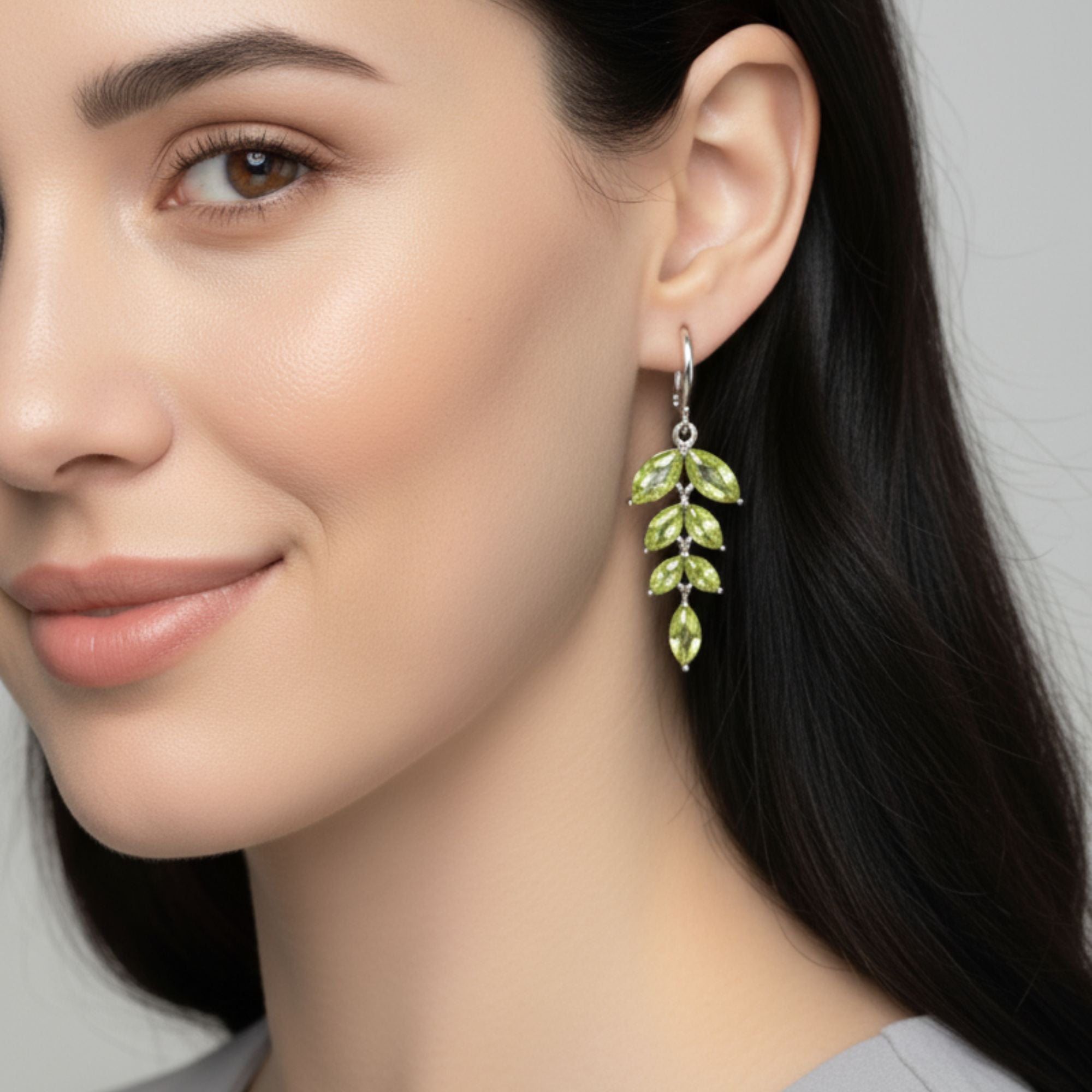 Close-up of a woman wearing green peridot leaf-shaped earrings with a neutral background