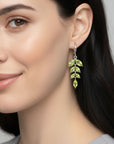 Close-up of a woman wearing green peridot leaf-shaped earrings with a neutral background