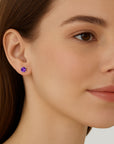 Close-up of a woman wearing a purple amethyst gemstone earring on a plain background