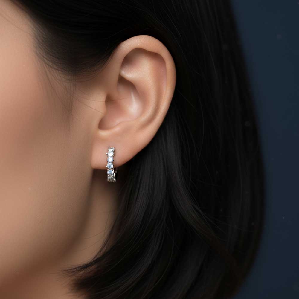 Close-up of an ear wearing a silver hoop earring with a dark background