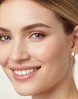 Close-up of a woman's face wearing a gold earring with a green gemstone on a beige background