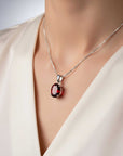 Silver necklace with a red gemstone pendant on a mannequin wearing a white blouse.