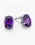 Pair of oval-cut vibrant purple amethyst stud earrings in a four-prong silver setting with push-back closures, displayed on a white background.
