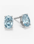 Pair of oval-cut light blue aquamarine stud earrings in a four-prong silver setting with push-back closures, displayed on a white background.