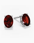 Pair of oval-cut deep red garnet stud earrings set in silver prong settings with push-back closures, displayed on a white background.