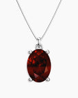 Oval-cut deep red garnet pendant in a four-prong silver setting, hanging from a silver box chain necklace, displayed on a white background