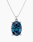 Oval-cut deep blue London topaz pendant in a four-prong silver setting, suspended from a fine silver chain, displayed on a white background.
