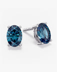 Pair of oval-cut deep blue London topaz stud earrings in a four-prong silver setting with push-back closures, displayed on a white background.