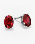 Pair of oval-cut vibrant red ruby stud earrings in a four-prong silver setting with push-back closures, displayed on a white background.