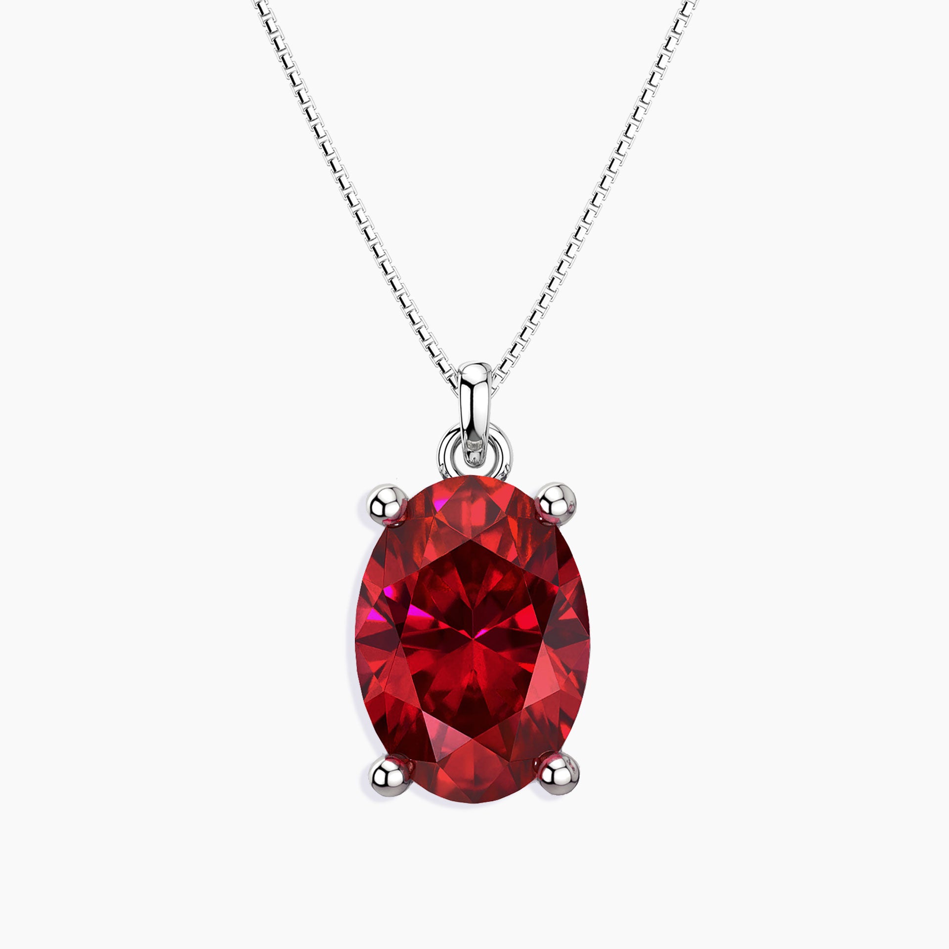 Oval-cut vibrant red ruby pendant in a four-prong silver setting, hanging from a fine silver chain, displayed on a white background