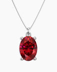 Oval-cut vibrant red ruby pendant in a four-prong silver setting, hanging from a fine silver chain, displayed on a white background