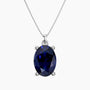 Oval-cut deep blue sapphire pendant in a four-prong silver setting, suspended from a fine silver chain, displayed on a white background.