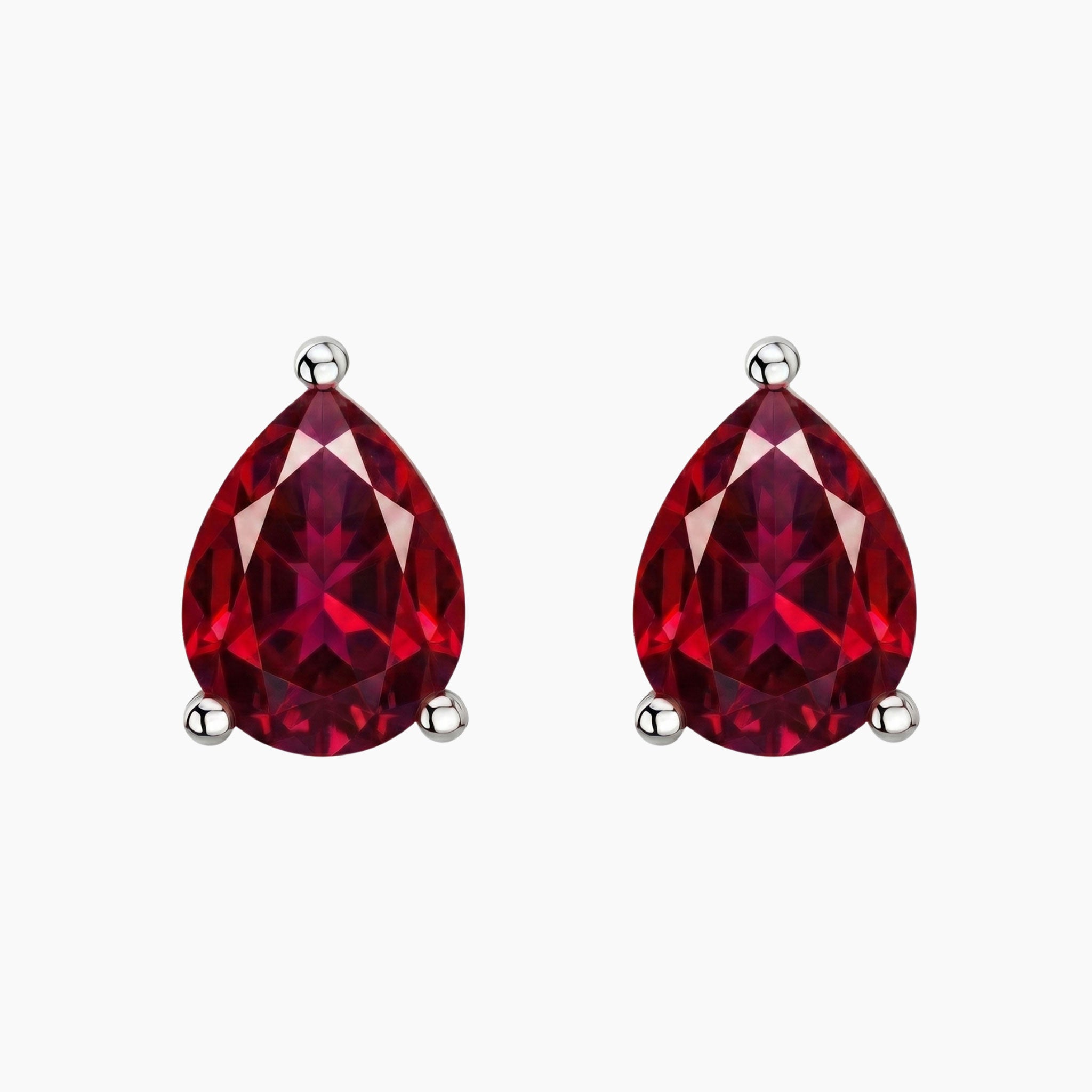 A pair of pear-shaped red ruby gemstone stud earrings in silver prong settings, shown on a plain light gray background.