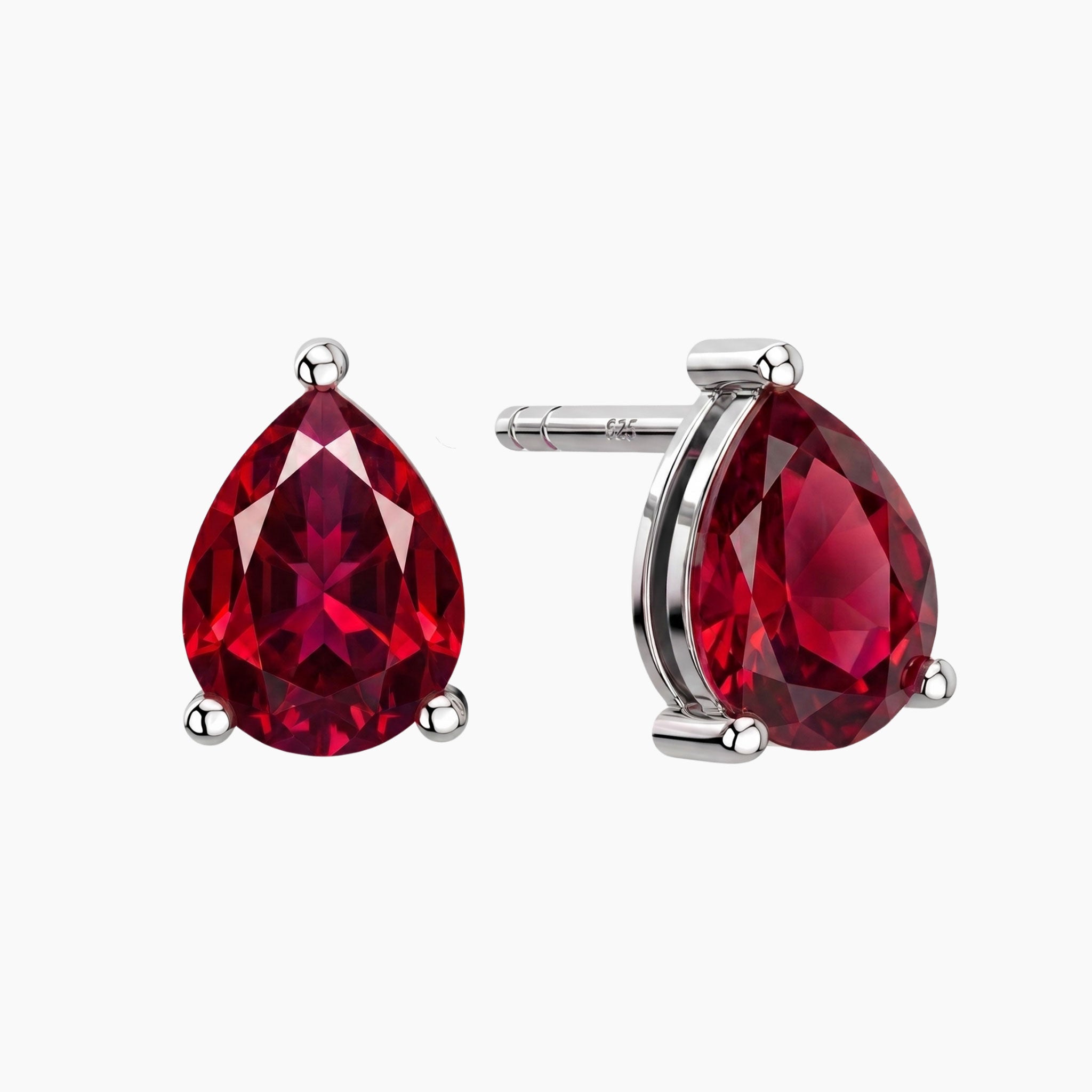 A pair of silver stud earrings featuring faceted teardrop-shaped deep red ruby gemstones, shown on a light gray background with one earring facing forward and the other showing the side profile and post.