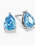 A pear-shaped Swiss blue topaz pendant in a three-prong sterling silver setting with a V-shaped bail, hanging from a fine silver box chain; the gemstone sparkles with bright sky-blue hues against a white background.
