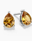 Two pear-shaped citrine stud earrings in sterling silver three-prong settings—one facing forward and the other angled slightly—featuring vibrant golden-yellow gemstones with brilliant facets, displayed on a clean white background.

