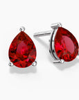 Two pear-shaped deep red gemstones set as sterling silver stud earrings, one shown head-on and the other at a slight angle, each held by three polished prongs on a clean white background.