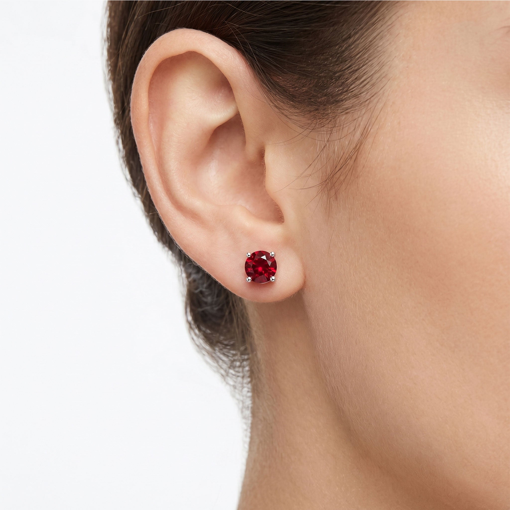 Close-up of an ear wearing a red ruby gemstone earring on a plain background