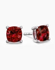 Cushion-cut ruby stud earrings in sterling silver, featuring rich red gemstones secured in a four-prong setting.