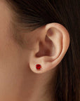 Close-up of an ear wearing a cushion-cut ruby stud earring in a 925 sterling silver four-prong setting