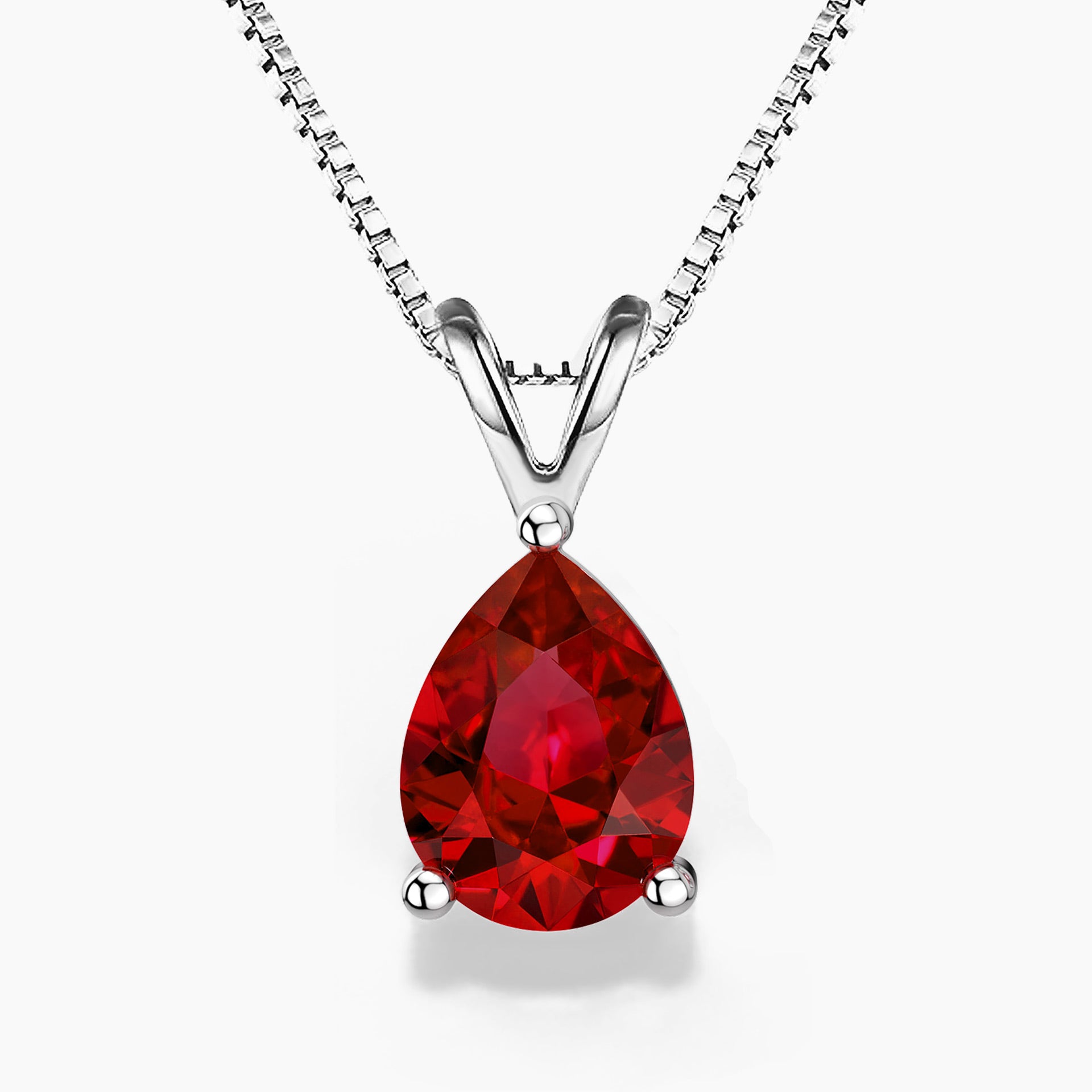 A pear-shaped deep red gemstone pendant set in polished sterling silver, hanging from a delicate silver chain against a white background.