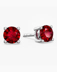 Pair of sterling-silver stud earrings set with round, faceted red rubies—one shown face-on, the other tilted to reveal its four-prong setting and the “S925” hallmark on the post—against a white background.