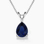 Alt: A pear-shaped deep-blue sapphire gemstone pendant in a sleek three-prong sterling silver setting, hanging from a delicate silver box chain with a V-shaped bail on a white background.
