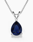 Alt: A pear-shaped deep-blue sapphire gemstone pendant in a sleek three-prong sterling silver setting, hanging from a delicate silver box chain with a V-shaped bail on a white background.
