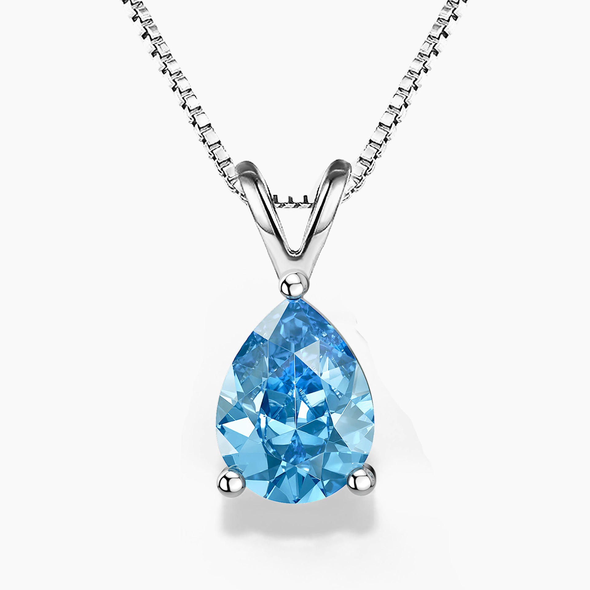A  pear-shaped Swiss blue topaz pendant in a three-prong sterling silver setting with a V-shaped bail, hanging from a delicate silver box chain on a white background; the gemstone features vibrant sky-blue hues with brilliant faceting.
