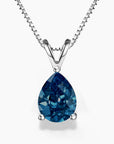A pear-shaped London blue topaz pendant set in a three-prong sterling silver setting with a V-shaped bail, suspended from a delicate silver box chain; the gemstone showcases deep ocean-blue tones with brilliant faceting, against a white background.
