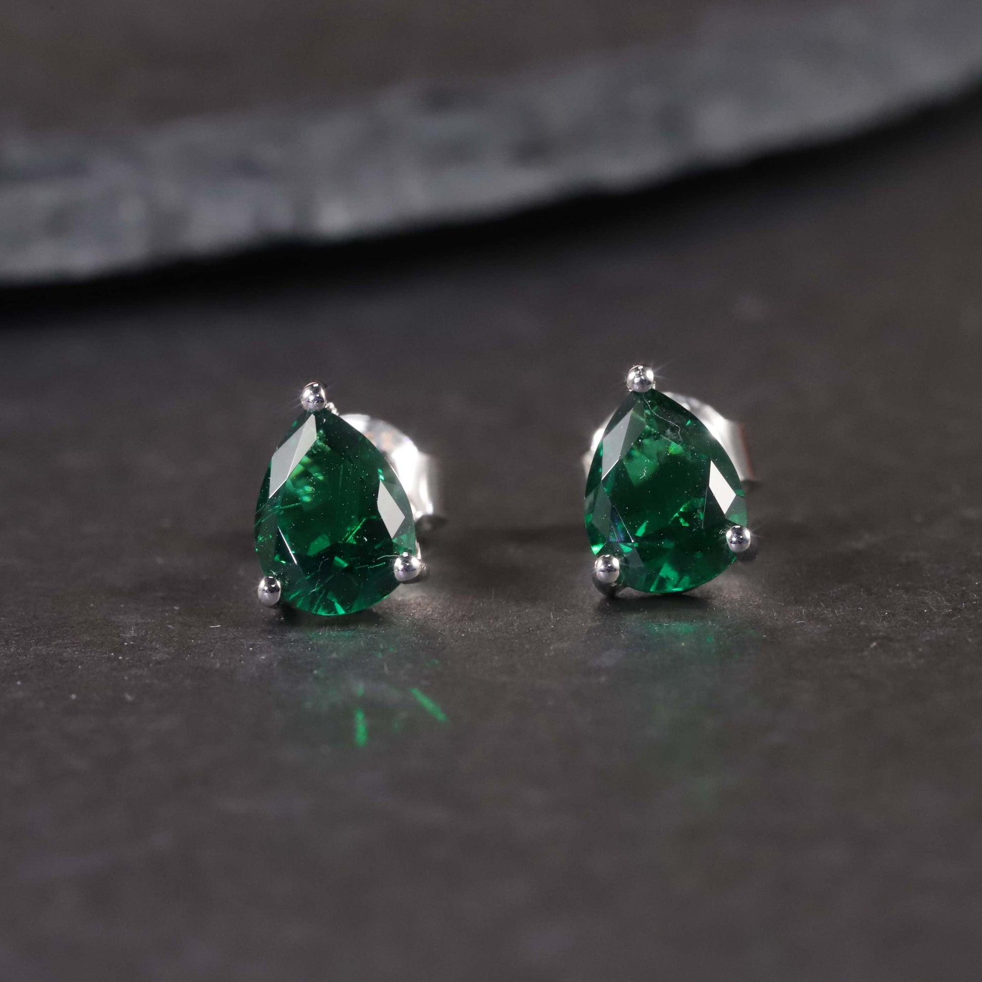 view of silver emerald pear cut stud earrings on dark background